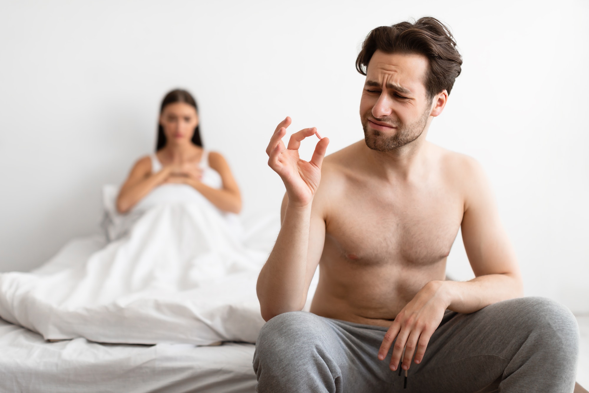 Unhappy Man Holding Potency Pill Before Sex In Bedroom Indoors